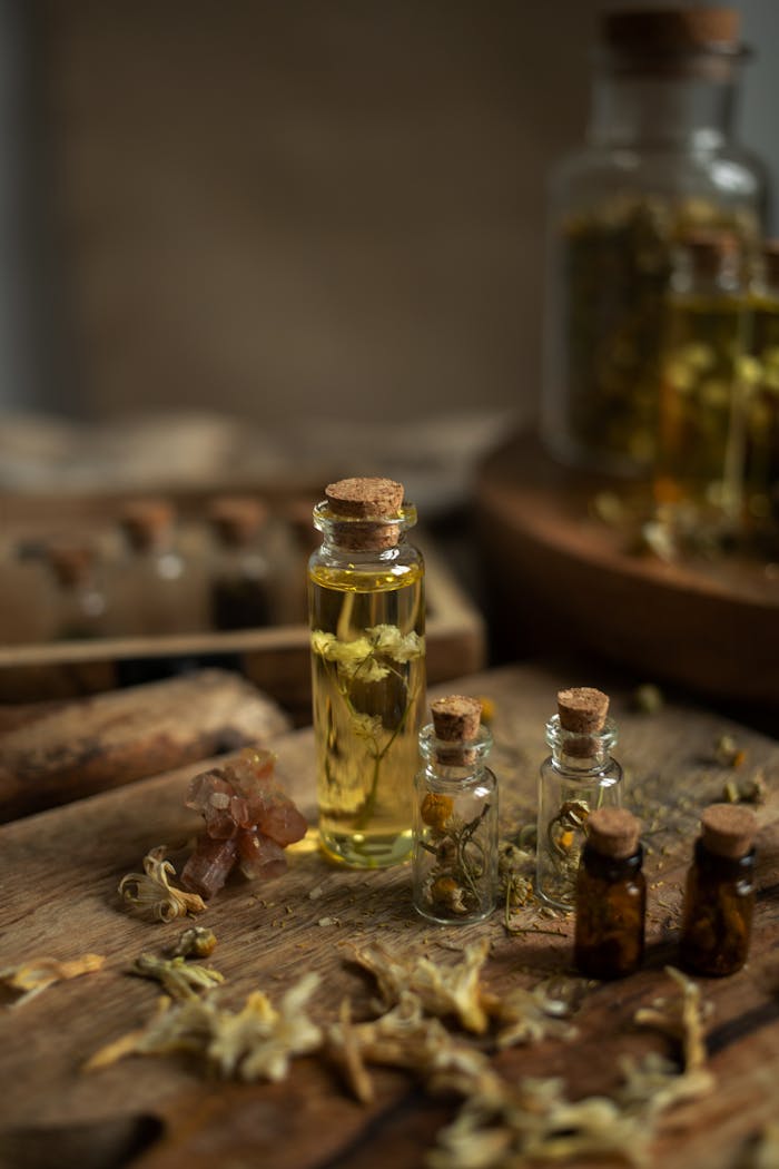 A collection of glass bottles filled with botanical oils on a rustic wooden surface, surrounded by dried flowers and herbs.